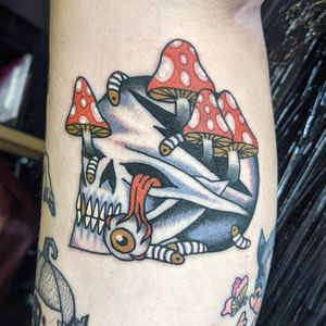 Get inked with a striking traditional tattoo featuring a skull and mushroom motif by the talented artist Benji Charnock.