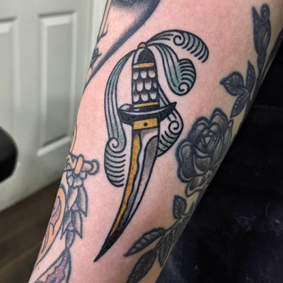 Get a bold and timeless traditional dagger tattoo by the talented artist Benji Charnock. Perfect for those who appreciate classic tattoo designs.