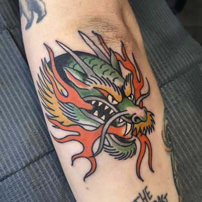 Get inked with a fierce traditional dragon design by renowned artist, Benji Charnock. This bold and timeless piece will make a powerful statement.