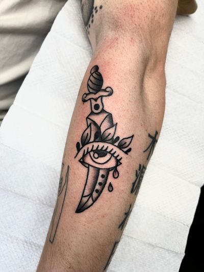 This traditional style tattoo features a menacing dagger piercing through a watchful eye, expertly executed by Clara Colibri.