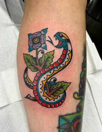 Exquisite traditional tattoo featuring a snake and flower motif by the talented artist Clara Colibri. Bold colors and intricate details make this design truly stand out.