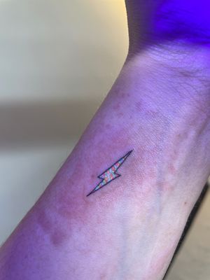 Get electrifying with this unique UV bolt tattoo in fine line style by talented artist Vera. Stand out with neon colors that pop under blacklight.