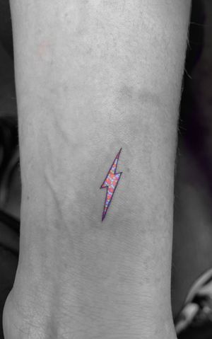 Experience the electrifying glow of a neon bolt tattooed with fine lines and UV ink, created by skilled artist Vera.