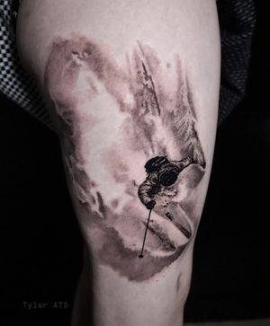 Skier slashing powder thigh tattoo. Soft black and grey realism.