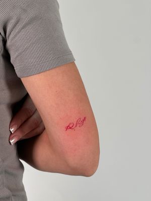 Get a striking red small lettering tattoo by Saka Tattoo for a subtle yet powerful design that showcases your unique style.