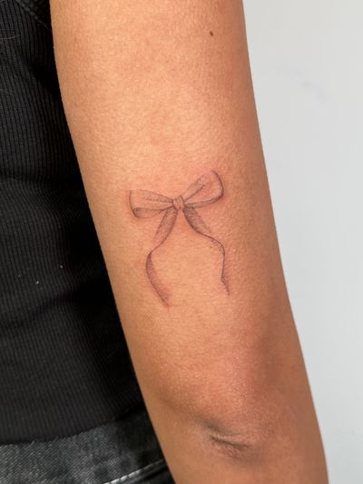 Hand-poked black and gray dotwork tattoo by Alina Wiltshire, featuring a delicate bow motif for a sophisticated look.