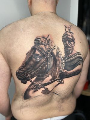 Experience the power and grace of a knight mounted on a majestic horse in this stunning black and gray tattoo by Gaston Gromnicki.