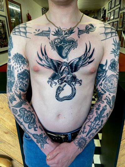 Get inked with an iconic traditional piece by flashbyaj featuring a snake, eagle, dagger, and sacred heart motif.