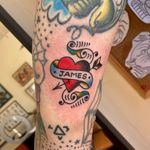 Get a timeless traditional tattoo featuring a heart, arrow, banner, and your name by the talented artist Flashbyaj.