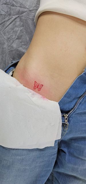 Elegant fine line butterfly tattoo in striking red ink, beautifully crafted by Larisa Andreea Boboc.