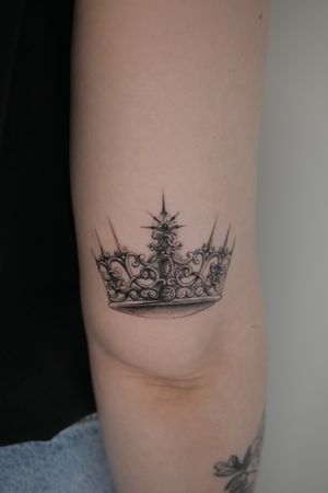 A stunning black and gray crown tattoo by Alexander Rufio, featuring intricate details and realism in a small design.