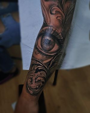 Beautiful black and gray illustrative tattoo featuring intricate filigree around a stunning eye, by Larisa Andreea Boboc.