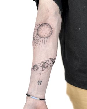 Experience the beauty of the cosmos with this stunning black and gray illustrative tattoo featuring a sun, planet, and solar system. By artist Bradley Mollett.