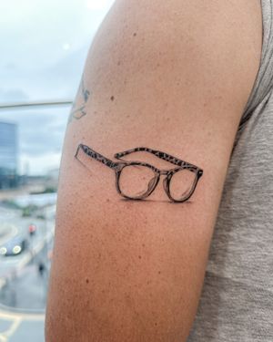 Experience meticulous artistry with this black and gray micro realism tattoo of glasses by the talented Bradley Mollett.