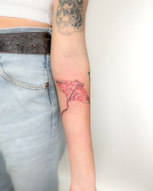 Bradley Mollett's illustrative tattoo features a delicate red origami ray design, resembling porcelain artistry.