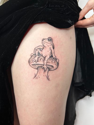 Enjoy a whimsical and nature-inspired tattoo featuring a frog and mushroom by talented artist Jonathan Glick.