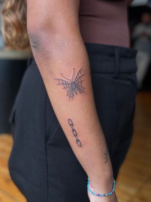 Fine line tattoo by Julia Bertholdi featuring a delicate butterfly connected by a chain. A stunning and unique design.