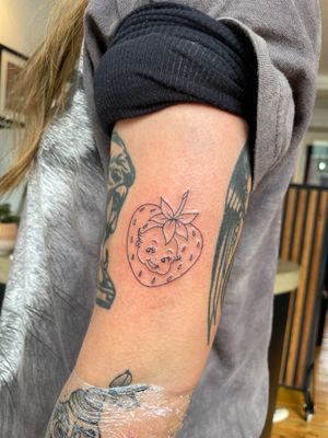 Delicate fine line and illustrative tattoo of a cute baby cuddling a strawberry, professionally done by Julia Bertholdi.