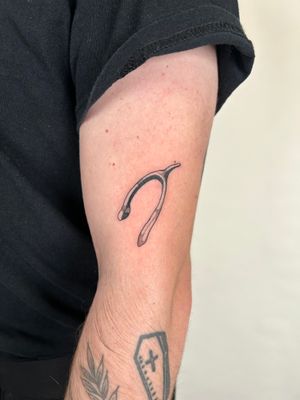 This black and gray dotwork tattoo by Jack Howard features a detailed illustrative design of a wishbone.