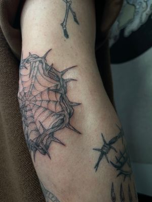 Get tangled in this illustrative tattoo featuring a web intertwined with thorns, expertly designed by Julia Bertholdi.