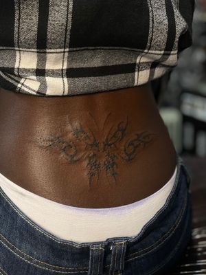 Discover the beauty of tribal art with this dark skin butterfly tramp stamp tattoo by Julia Bertholdi.