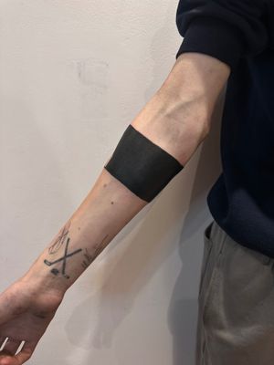 This striking blackout band tattoo by Oliver Soames features a sleek and modern blackwork design.