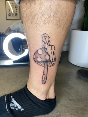 Get a unique black and gray illustrative tattoo of a pin up girl with a mushroom by the talented artist Charlie Macarthur.