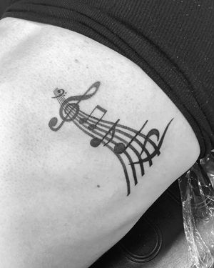 Express your love for music with this detailed illustrative tattoo featuring music notes and partiture. Designed by the talented artist Ronny East.