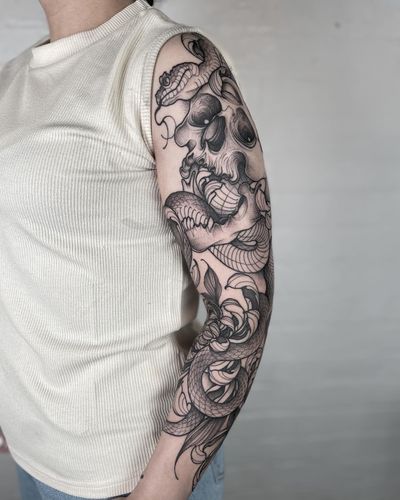Get a stunning blackwork tattoo featuring a snake, flower, and skull motif, expertly done by Claudia Smith.