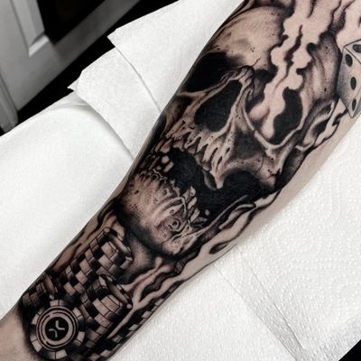 Intricate black and gray tattoo featuring a skull surrounded by casino chips and dice, expertly done by Liam Harbison.