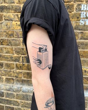 Get inked with a unique blackwork tattoo of a grater, symbolizing your passion for cooking. Done by Dave Norman.