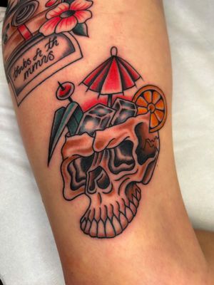 Check out this classic traditional tattoo featuring a skull and drink motif, expertly done by artist Barney Coles.