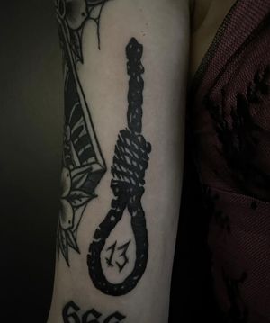 Experience the haunting beauty of this blackwork tattoo featuring a rope, gallows, and hanging rope design by the talented artist Sophia Hayes.
