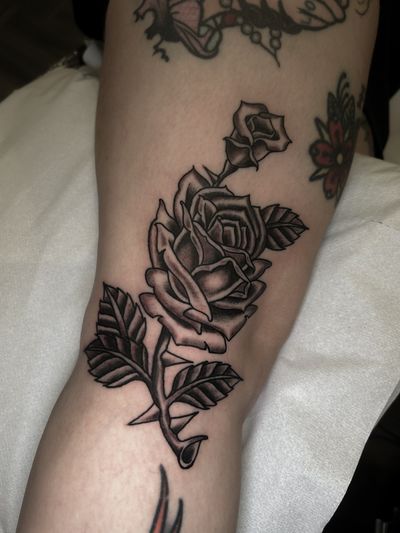 Experience the timeless beauty of a traditional black and gray rose tattoo expertly crafted by renowned artist Barney Coles.