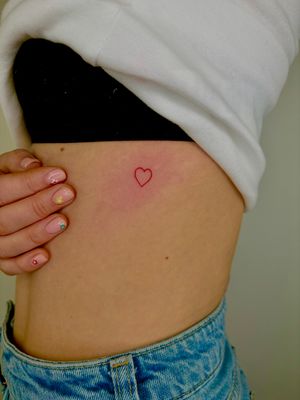 Elegant and minimalist fine line heart tattoo in striking red ink by Ruth Hall. Perfect for those seeking a timeless symbol of love.