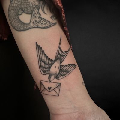 Beautiful tattoo design by Jenny Dubet featuring a swallow carrying a love letter. Perfect for those who want a romantic tattoo with a touch of nostalgia.