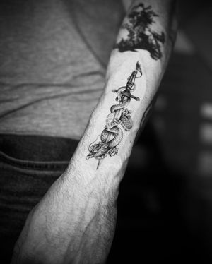 By Georgina, this impressive tattoo features a fierce dragon intertwined with a sharp dagger in a striking black and gray style.