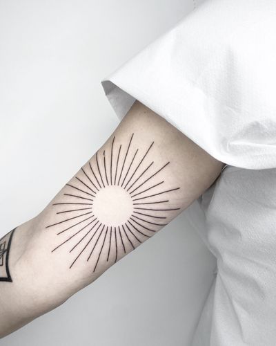 Featuring fine line work and sleek geometric patterns, this tattoo of a stylized sun by Malvina Maria Wisniewska is a modern take on a classic motif.