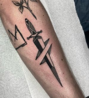 Get a timeless and bold traditional dagger tattoo by renowned artist Ryan Goodrum. Perfect for those who appreciate classic tattoo motifs.
