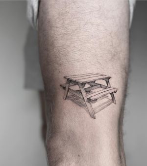 Illustrative black and gray tattoo of a serene park bench, skillfully done by Kayla.
