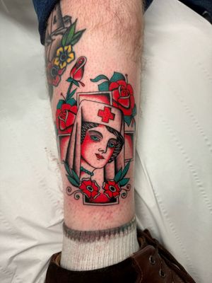 Get inked with a stunning traditional tattoo featuring a beautiful rose, nurse symbol, and playing cards motif by Ryan Goodrum.
