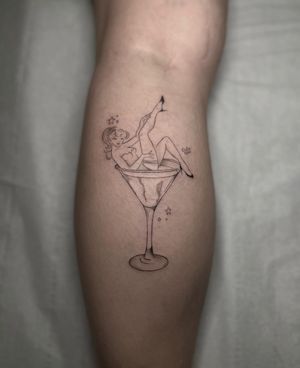 A fine line tattoo of a sultry pin up girl holding a martini glass, beautifully designed by Maddie.