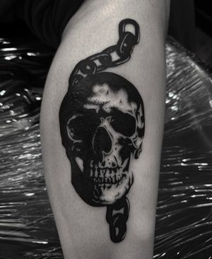 Experience the dark allure of Sophia Hayes' illustrative blackwork tattoo featuring a striking skull intertwined with chains.