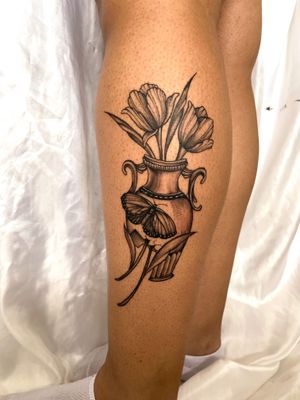 Beautifully detailed tattoo featuring a butterfly, flower, and vase in stunning black and gray illustrative style. Created by the talented artist, Gabriela.