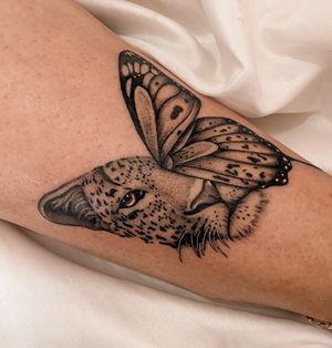 Experience the beauty of nature with this black and gray illustrative tattoo featuring a leopard, butterfly, and jaguar. Created by the talented artist Gabriela.