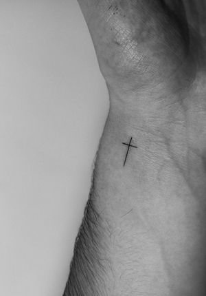 Elegant fine line tattoo of a delicate cross, expertly crafted by the talented artist Meg.