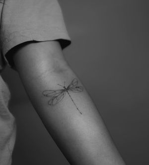Get a dainty and intricate dragonfly tattoo with fine line details and illustrative style by the talented artist Meg.