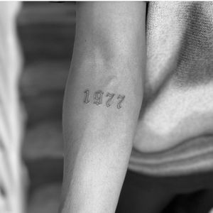 Get a small lettering tattoo of a significant date with delicate fine line work by Monike for a timeless and personal piece of body art.