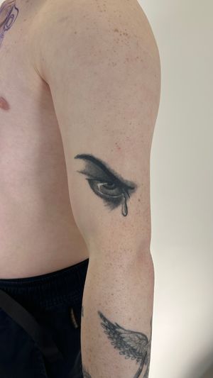 Illustrative black and gray tattoo of a sorrowful eye shedding a tear, done by Saka Tattoo.