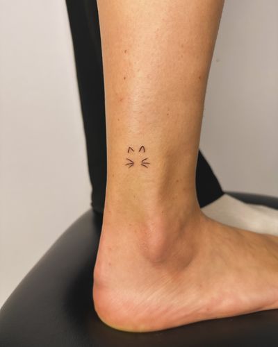Fine line and hand poke style tattoo of a cat outline, done by jadeshaw_tattoos. Simple yet elegant design.